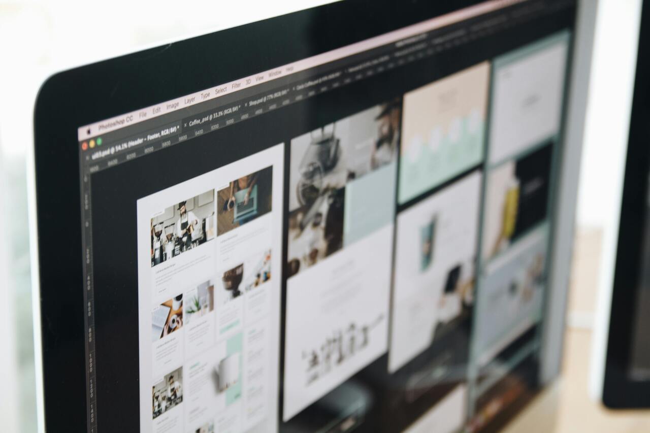Persoon werkt aan de ontwerpfase van een website met geprinte wireframes en laptop aan een bureau